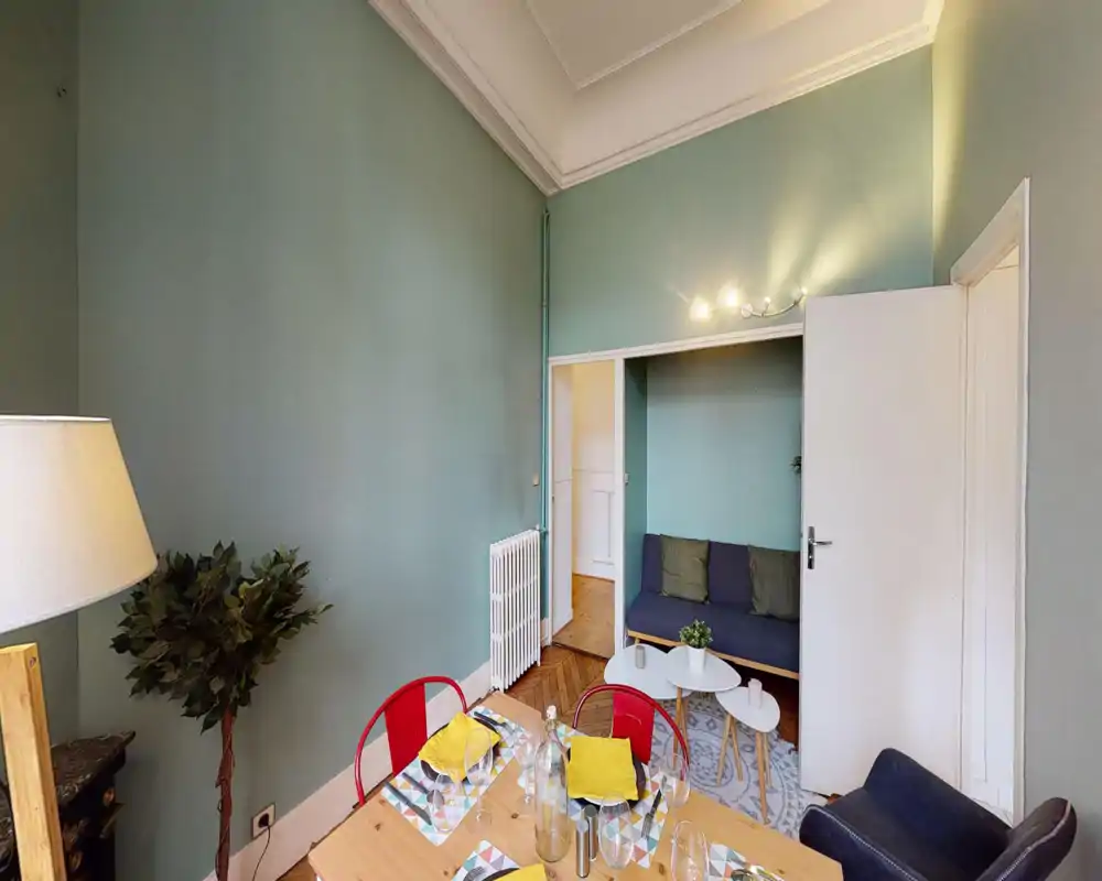 Bright, styled dining area with a set table and colorful chairs, opening onto a cozy seating nook — an inviting space for meals and small gatherings.