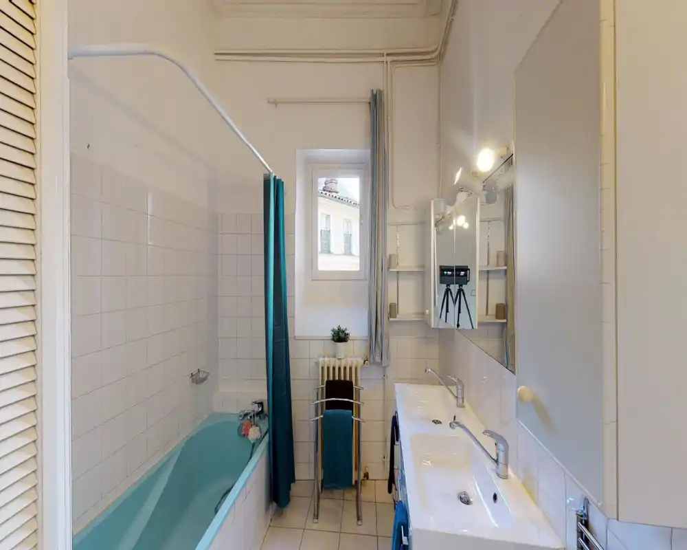 Bright, clean bathroom with a turquoise bathtub, double sink vanity, mirrored cabinet and tiled walls. A window provides natural light and a shower curtain separates the tub area.