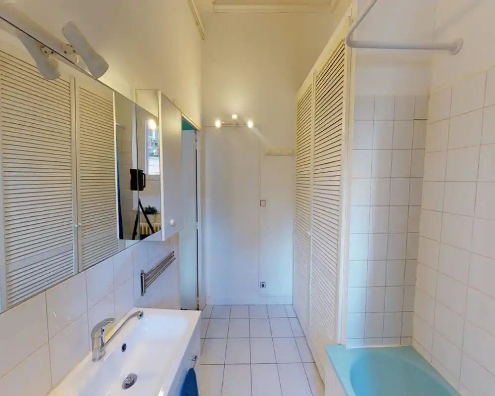 Bright, tidy bathroom with a sink, mirror cabinets and a built-in bathtub. White tiles and louvered storage doors give a clean, functional feel.