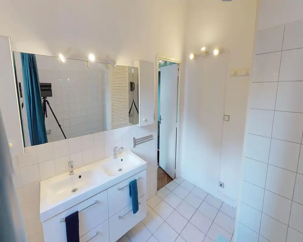 Bright tiled bathroom with a double sink vanity, large mirror and clean white finishes; modern spot lighting and towels add a neat, functional look.