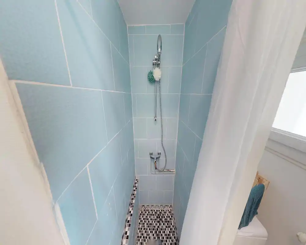 Compact tiled shower with blue wall tiles, handheld showerhead and a mosaic tile floor; simple, bright bathroom area ideal for a small rental.