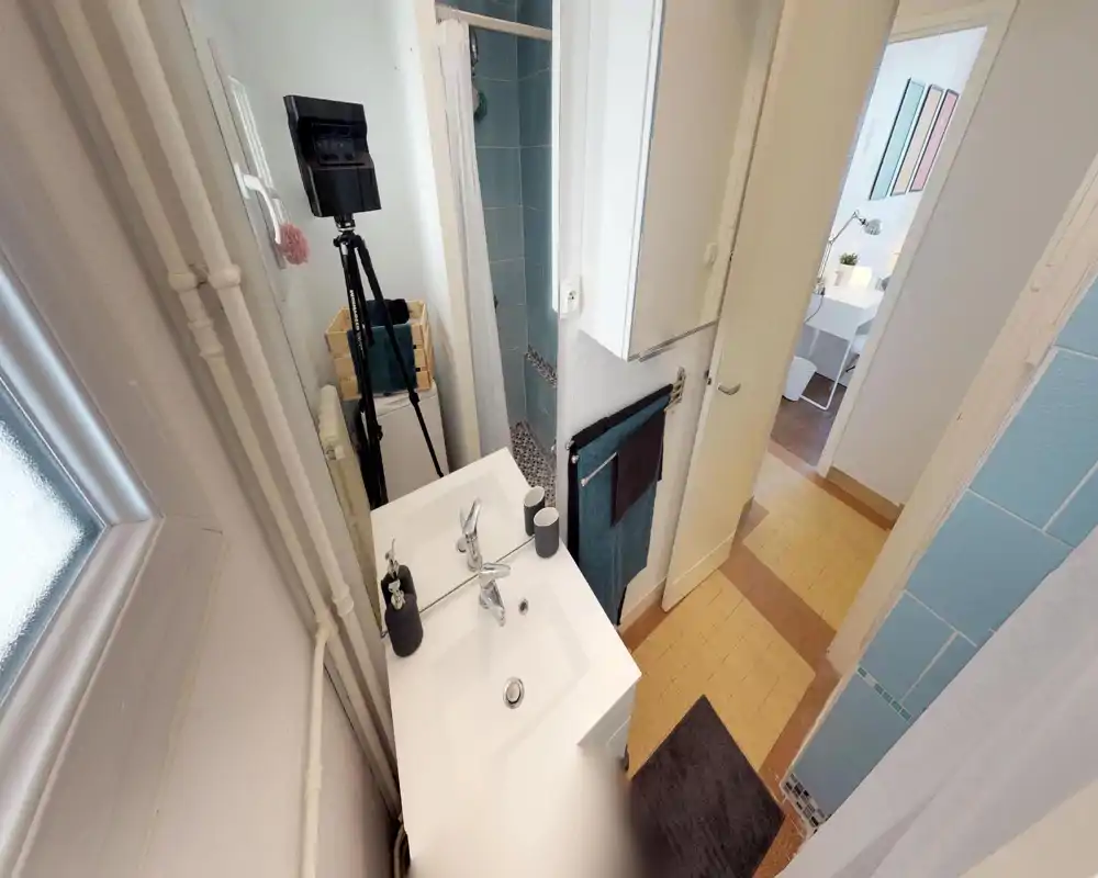 Compact bathroom with a white vanity sink, mirror, towel rack and shower stall with blue tiles; bright and tidy space suitable for a rental listing.