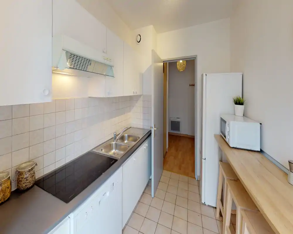 Bright, tidy galley kitchen with a double sink, induction hob, refrigerator and a wooden breakfast bar — ideal for compact city apartments.