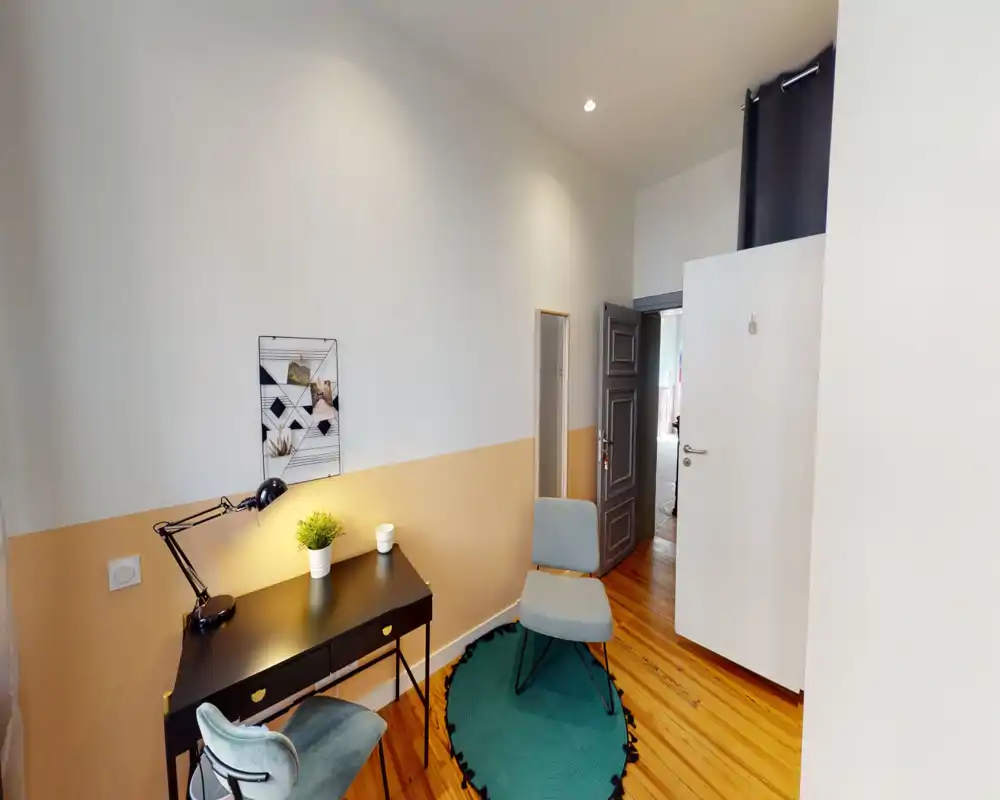 Coin salon chaleureux avec un petit bureau, un fauteuil et un tapis. Murs neutres et parquet chaleureux forment un espace agréable pour lire ou travailler.