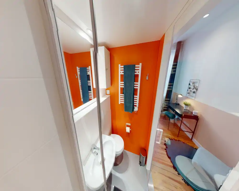 Salle de bains compacte et moderne avec un mur orange, radiateur porte-serviettes mural et lavabo et WC blancs ; lumineux et soigné.