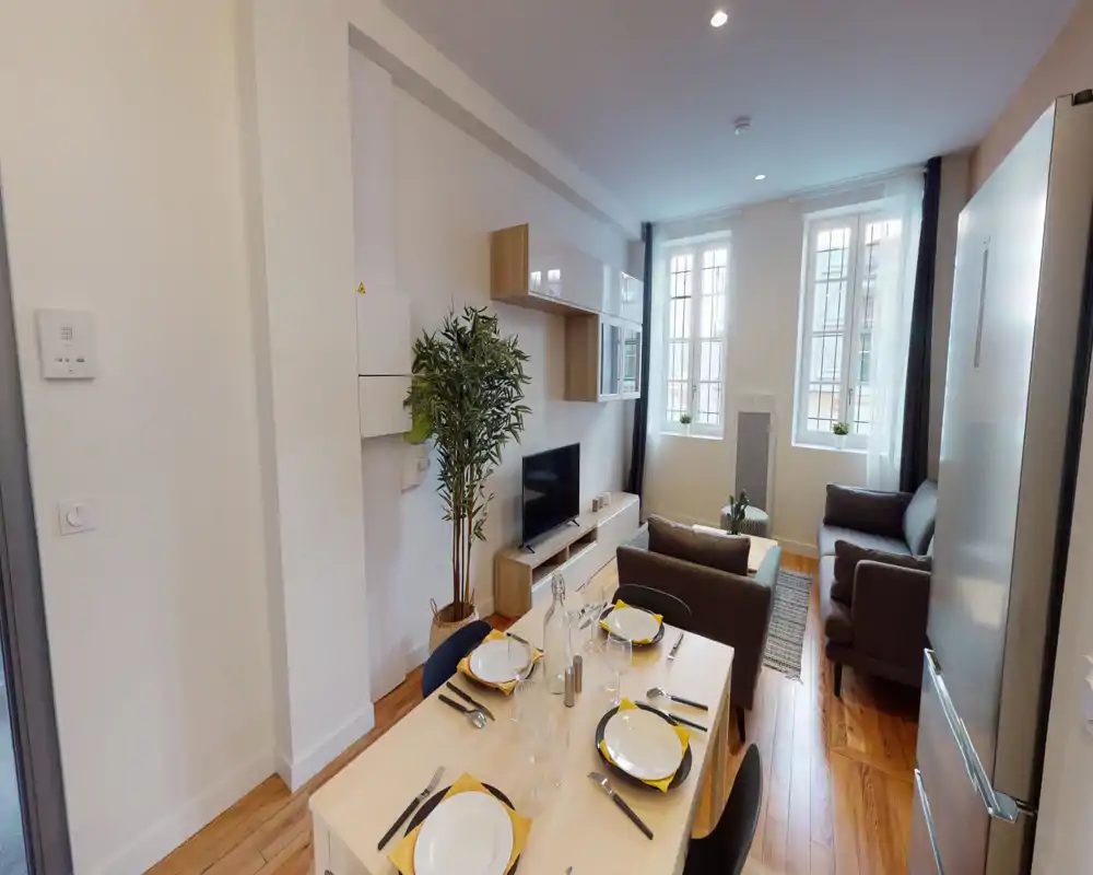 Salle de séjour moderne et ouverte, lumineuse, avec canapé confortable, meuble TV et table à manger dressée pour quatre personnes — idéale pour un séjour en ville.