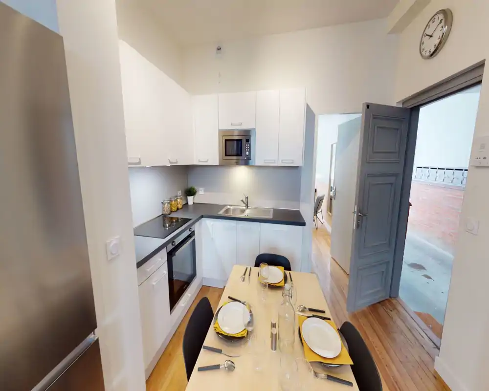 Cuisine moderne et compacte avec placards blancs, four et micro-ondes intégrés, évier sous éclairage d'ambiance et petite table dressée pour quatre — idéale pour une location urbaine conviviale.