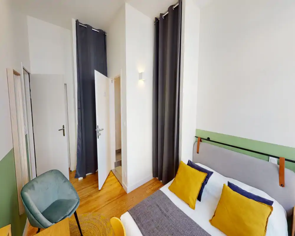 Camera da letto luminosa e curata con letto doppio comodo, cuscini decorativi e pavimento in legno; arredamento moderno e luce naturale gradevole.