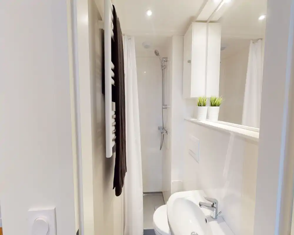 Bagno compatto e moderno con doccia, piastrelle bianche, lavabo e mobile a parete. Pulito, luminoso e ottimizzato per spazi ridotti.
