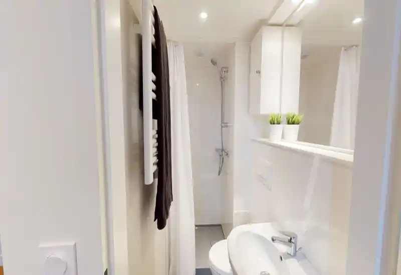 Bagno compatto e moderno con doccia, piastrelle bianche, lavabo e mobile a parete. Pulito, luminoso e ottimizzato per spazi ridotti.