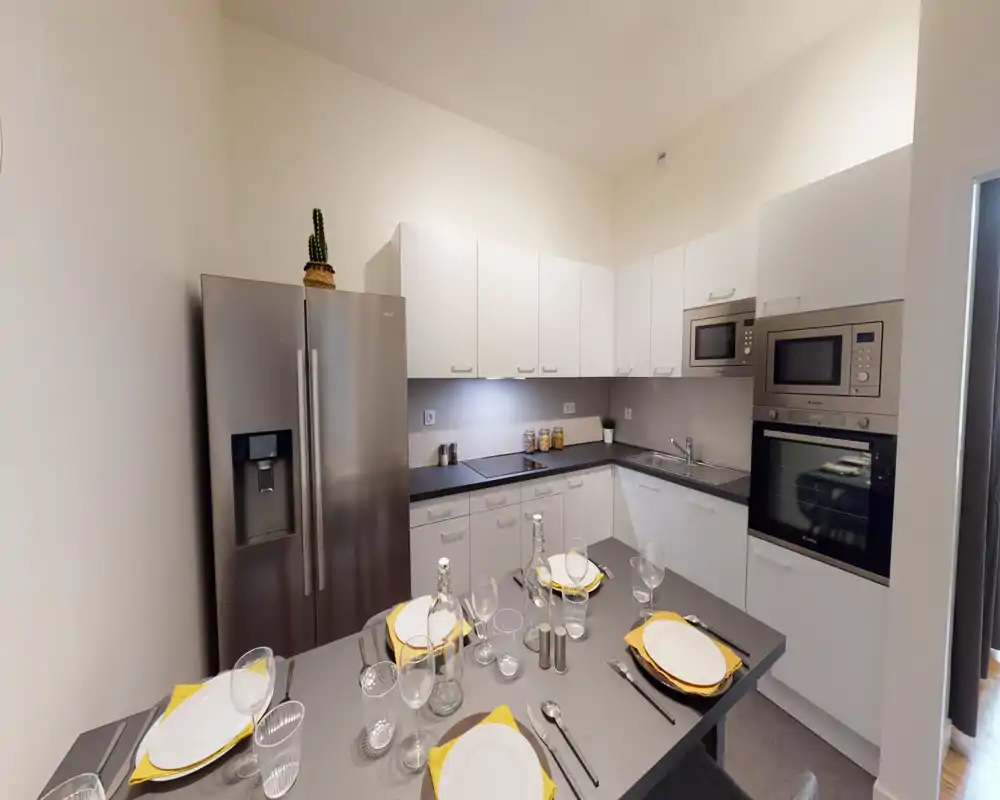 Cucina moderna completamente attrezzata con mobili bianchi, elettrodomestici in acciaio inox e tavola apparecchiata sull'isola — luminosa e ordinata.