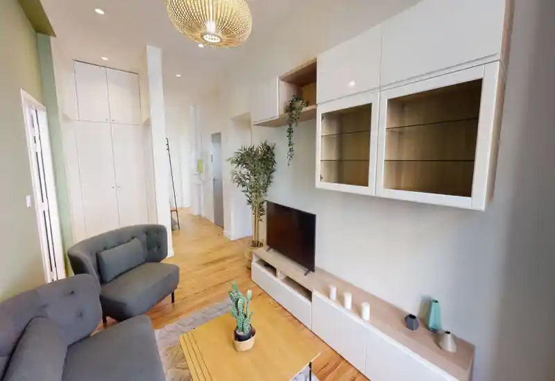 Soggiorno moderno e luminoso con divano grigio, poltrona abbinata, mobile TV e mensole decorative — pavimenti in legno e tessili morbidi rendono l'ambiente accogliente.