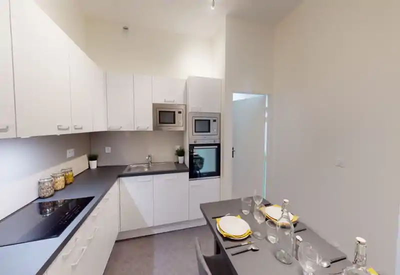 Cucina moderna e luminosa con mobili bianchi, forno e microonde integrati, piano cottura a induzione e un bancone apparecchiato — perfetta per appartamenti compatti in città.