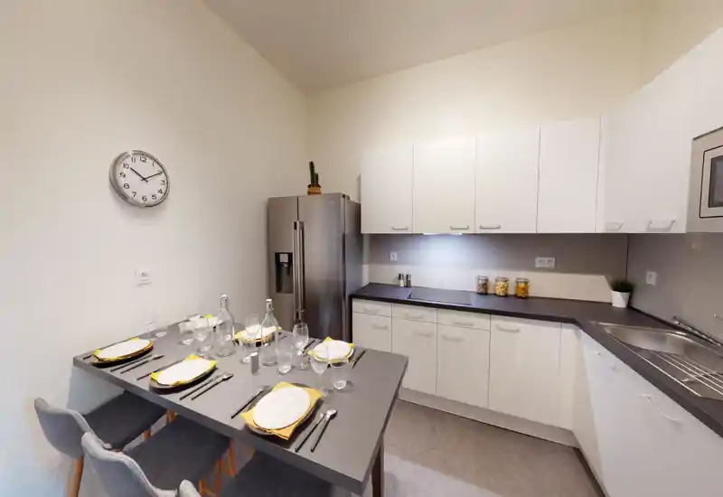 Cucina moderna e ben attrezzata con pensili bianchi, piani scuri, frigorifero in acciaio e tavolo da pranzo per quattro persone — luminosa e curata, ideale per affitti.