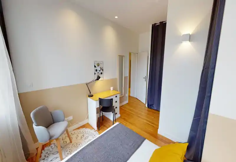Bright and well-styled bedroom corner with a visible bed, a small desk and a cozy armchair — ideal for work and relaxation. Soft natural light and warm wooden floors create a welcoming atmosphere.