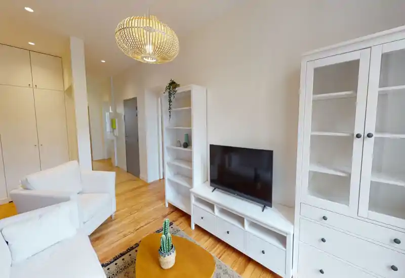 Soggiorno moderno e luminoso con divani bianchi, TV su mobile basso, librerie e pavimento in legno caldo — uno spazio accogliente e ben illuminato ideale per rilassarsi.