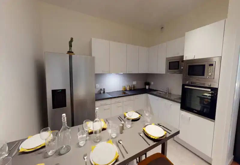 Cucina moderna ad angolo a forma di L con elettrodomestici in acciaio inox, forno e microonde integrati e bancone apparecchiato per quattro con stoviglie e tovaglioli gialli.