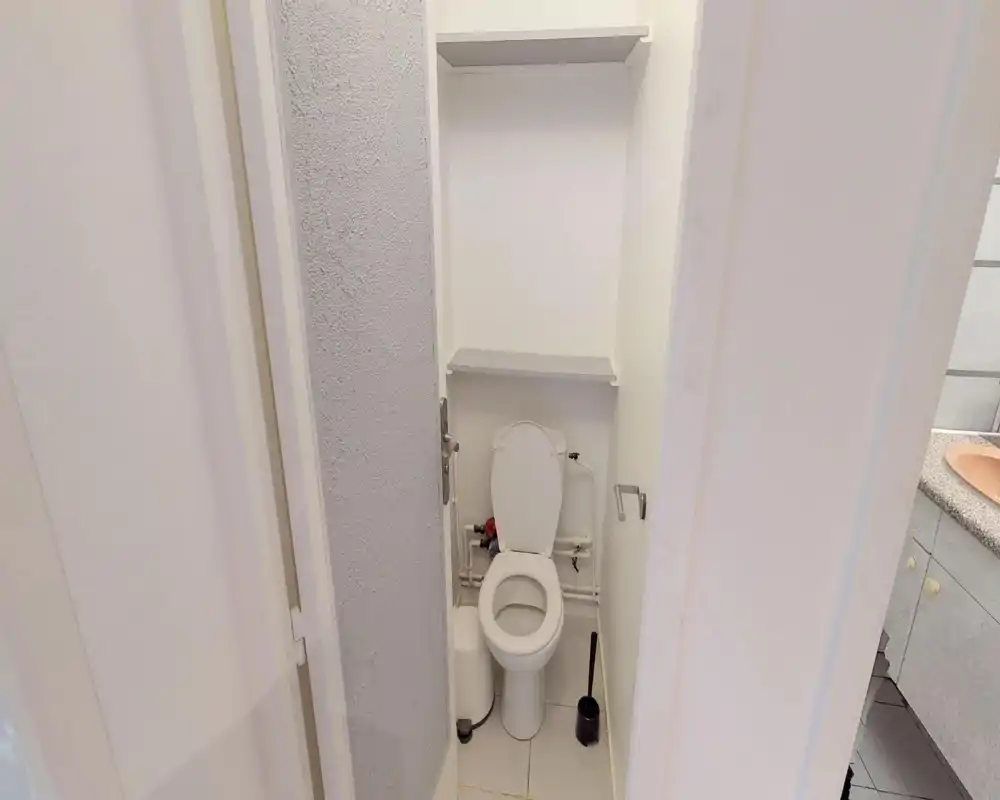 WC compatto con wc standard, scaffali a parete sopra lo sciacquone e accessori pratici; bagno piccolo, pulito e ben illuminato.