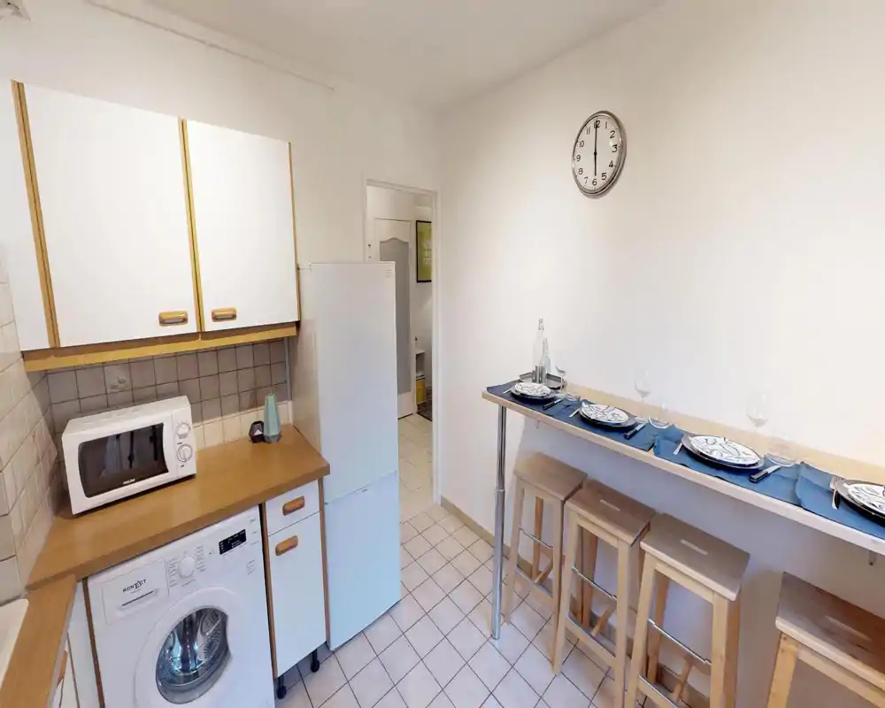Cucina compatta e luminosa con piano in legno, pensili bianchi, frigorifero e microonde; un bancone con sgabelli apparecchiato per la colazione.