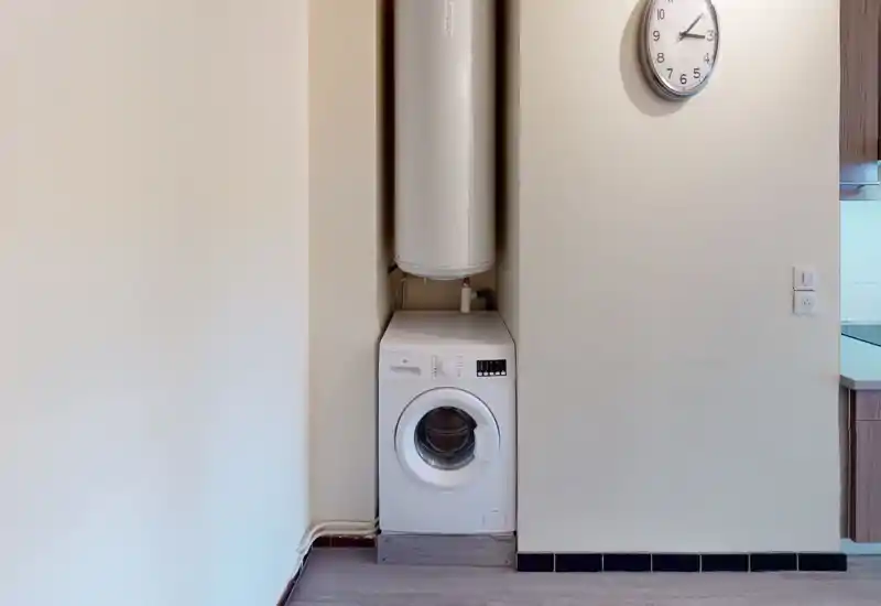 Angolo elettrodomestici compatto integrato nel muro della cucina: lavatrice a carica frontale sotto il boiler, in un angolo ordinato e ben illuminato accanto alla zona cucina.