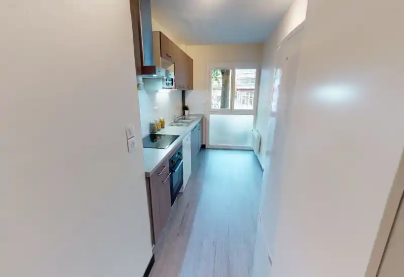 Cucina stretta e luminosa in stile moderno con pensili in legno, piano ad induzione, forno integrato e lavello sotto una finestra che garantisce luce naturale.