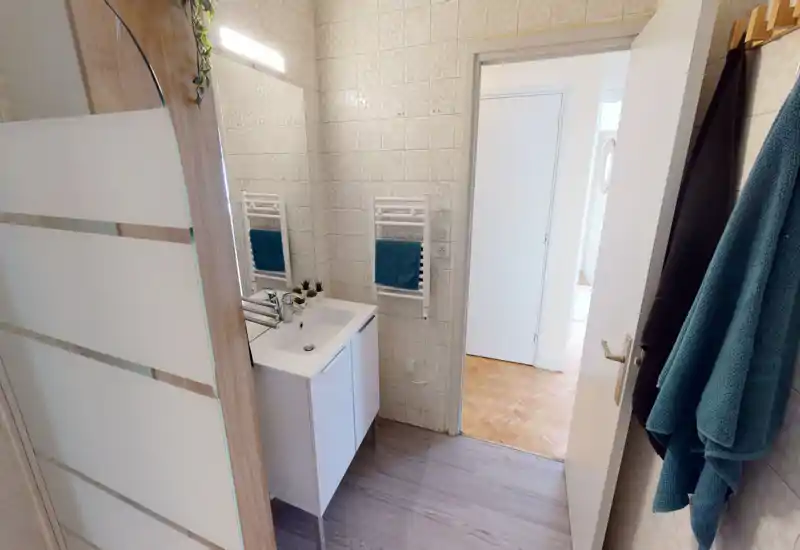 Bagno luminoso e ordinato con mobile lavabo bianco, termoarredo a parete e piastrelle con motivo; lo specchio e gli asciugamani turchesi donano un tocco fresco.