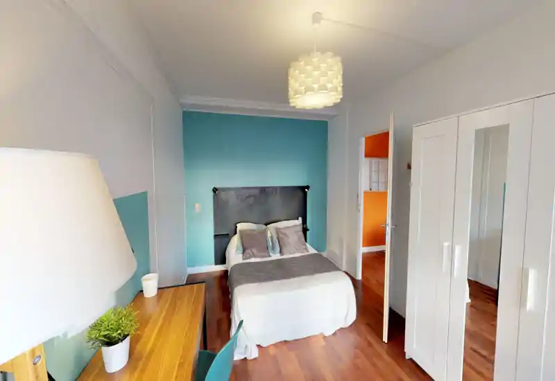 Bright, neatly staged bedroom with a double bed centered against a teal accent wall, wooden floors, a wardrobe with mirror, and a small desk—comfortable and ready for guests.