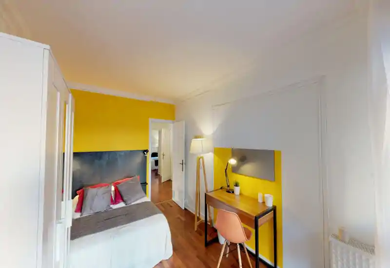 Bright, well-staged bedroom with a double bed, colorful yellow accent wall and a small wooden desk by the window — ideal for a cozy city stay.