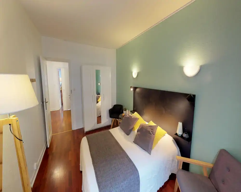 Bright, well-styled bedroom with a double bed, soft textiles and coordinating cushions. The room features a painted accent wall, bedside lighting and warm wooden flooring for a cozy atmosphere.