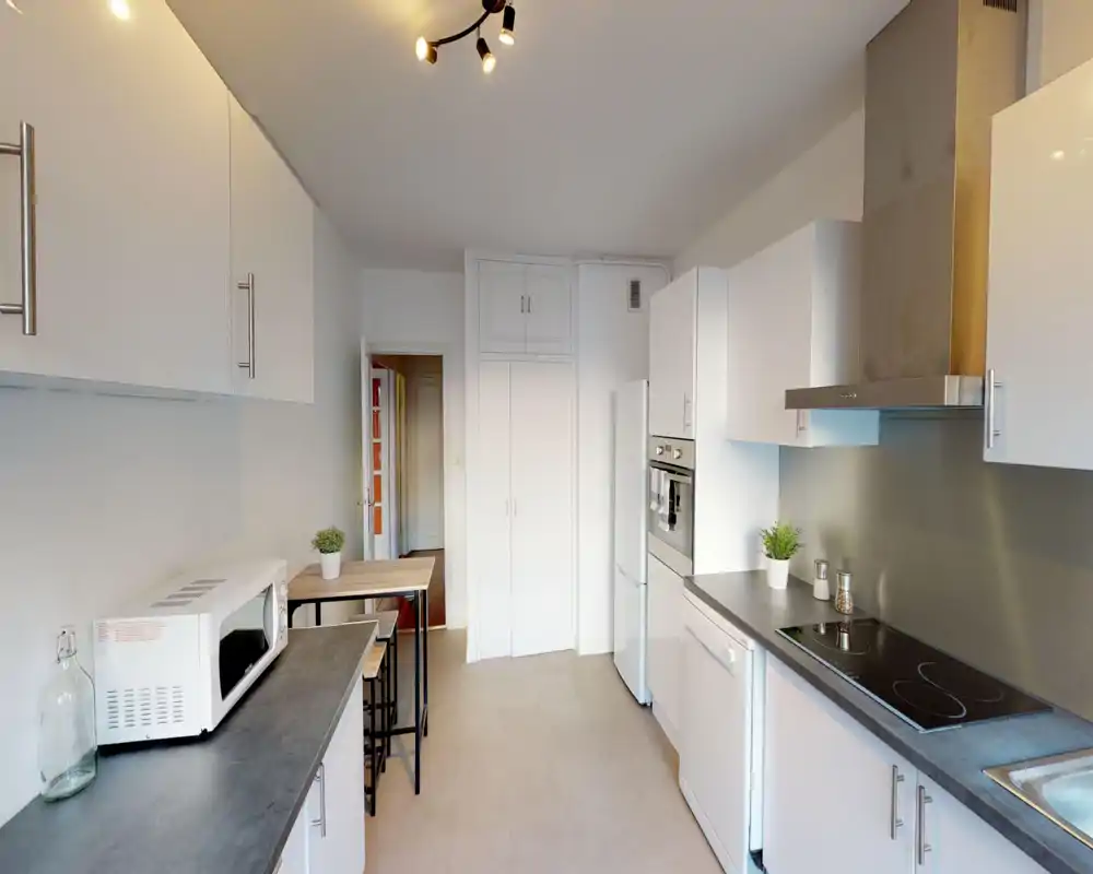 Bright, modern galley kitchen with white cabinets, integrated oven, ceramic hob and a compact breakfast table — tidy and functional for everyday cooking.