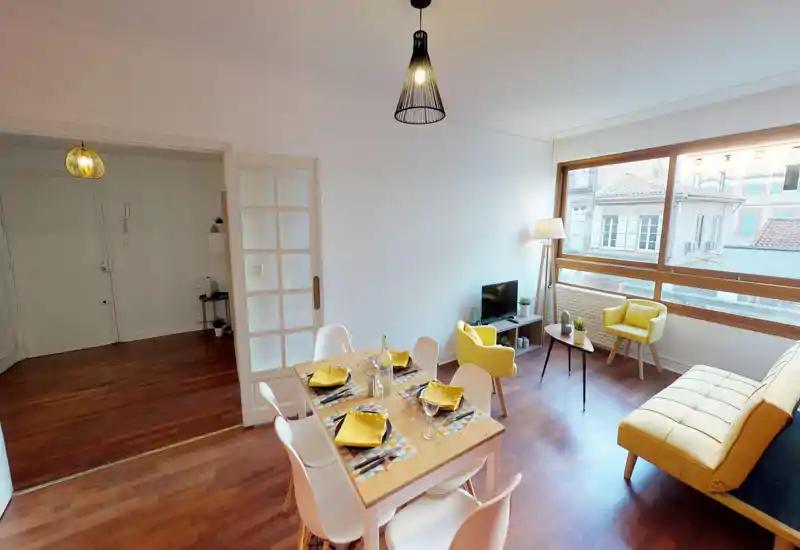 Bright, stylish living room with a large window, yellow accent seating and a dining table set for four — ideal for socializing and enjoying natural light.