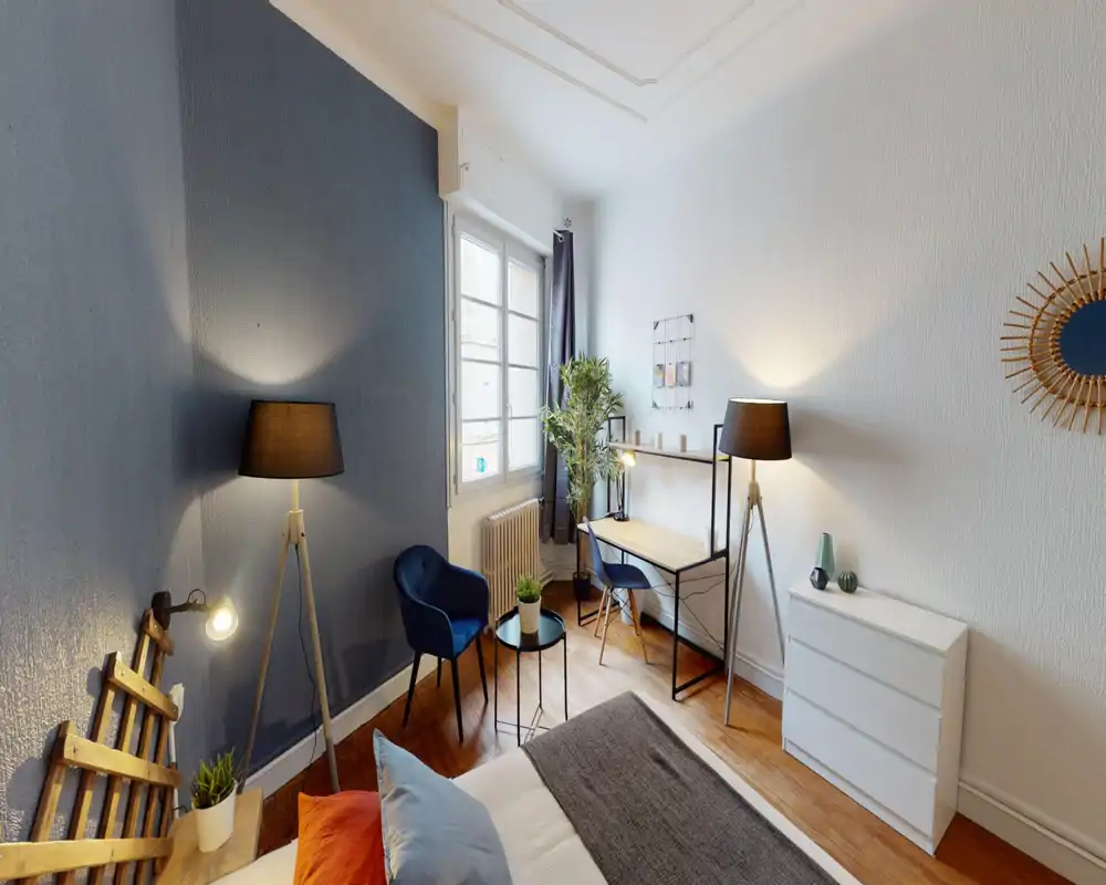 Bright, stylish bedroom with a comfortable bed in the foreground, a small desk by the window, armchairs and soft lighting creating a cozy atmosphere.