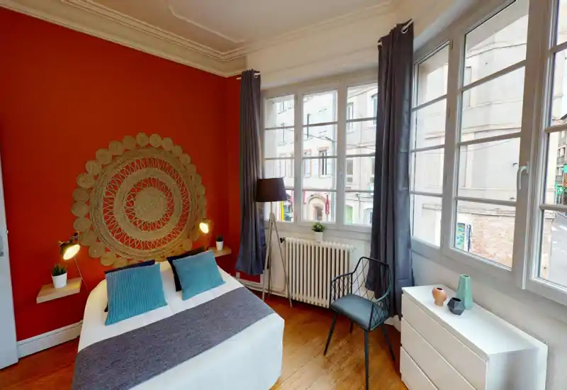 Chambre lumineuse et élégante avec un grand lit, une décoration murale texturée et de grandes fenêtres laissant entrer beaucoup de lumière naturelle.