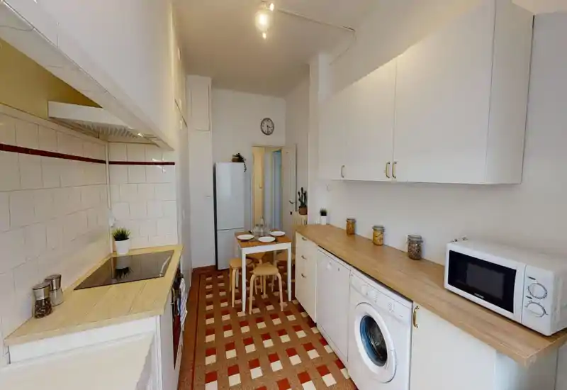 Cuisine lumineuse et étroite avec placards blancs, plans de travail en bois, électroménagers intégrés et petite table à manger — idéale pour un appartement citadin compact.