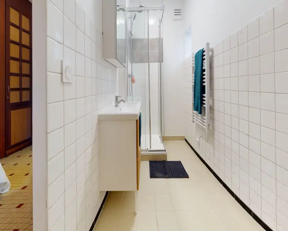 Bright, neatly tiled bathroom with a glass-enclosed shower, wall-mounted sink cabinet and heated towel rail. Clean, minimal styling ideal for rental listings.