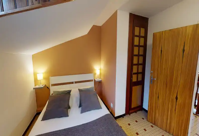 Bright, cozy attic bedroom with a white double bed, two bedside lamps and warm ochre accent wall — ideal for a restful stay.