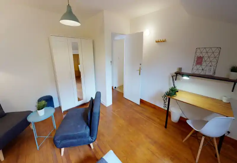 Bright, tidy living area with a small sofa, side table, wardrobe and a work desk — warm wooden floors and simple modern lighting create a comfortable multi-use space.