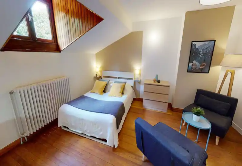 Bright, cozy attic bedroom with a double bed, warm bedside lamps and a small seating area — ideal for a comfortable stay.