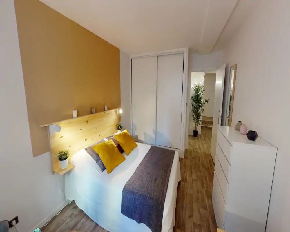 Bright, cozy double bedroom with a wooden headboard, mustard accent pillows and built-in wardrobe. Clean styling and warm lighting create an inviting atmosphere ideal for rental listings.