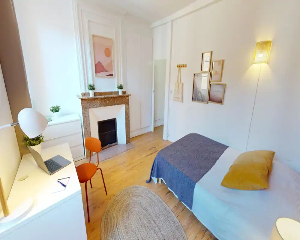 Camera da letto singola luminosa e accogliente con letto ben fatto, pavimento in legno, quadri decorativi e un piccolo angolo studio con scrivania e sedia. La luce naturale e le tonalità calde creano un ambiente ideale per affitti brevi o studenti.