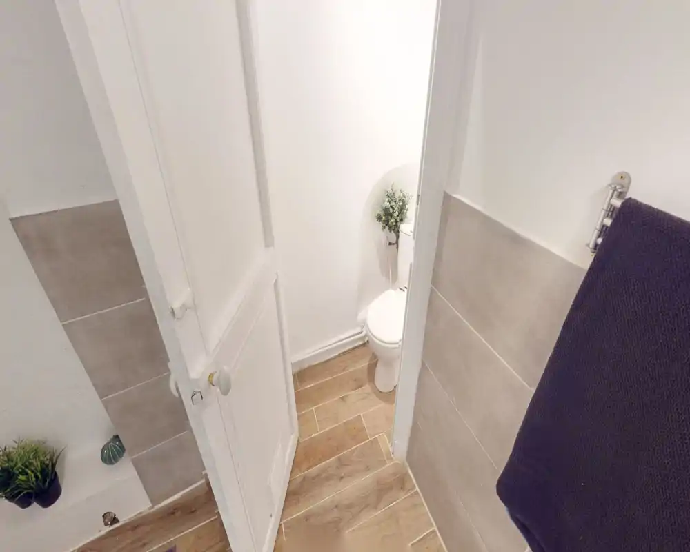 Bagno piccolo con WC visibile, pareti bianche e pavimento effetto legno; luminoso e ben curato.