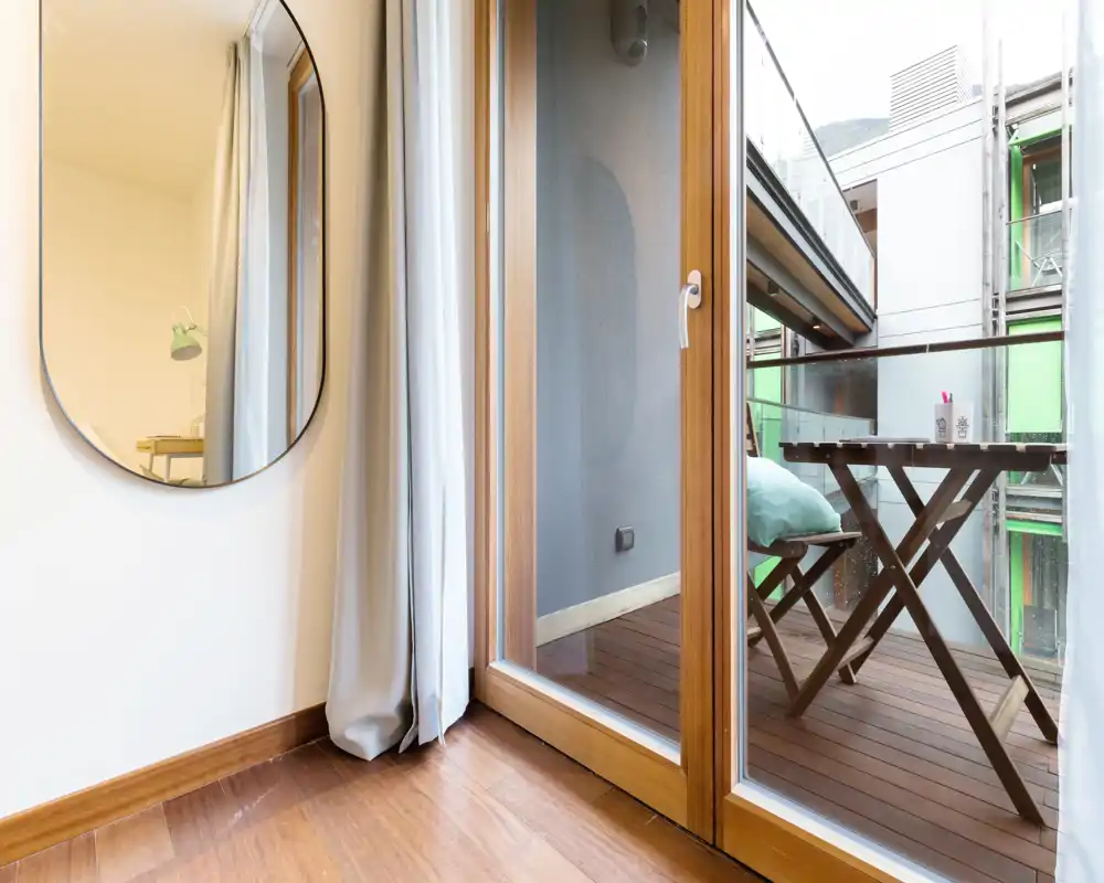 Small balcony with wooden decking and a folding table and chair set; bright natural light and a cozy cushion make it a pleasant outdoor spot.