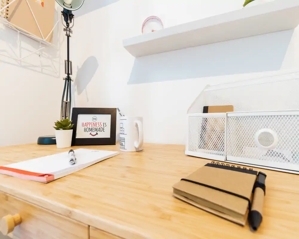 Bright, minimal workspace corner with a wooden desk, desk lamp, small plant and organized accessories — ideal for focused work or study.