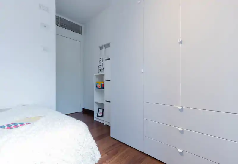 Minimalist bedroom view with a cosy textured bedspread, white built-in wardrobe and warm wooden floor; clean, bright and suitable for rental listings.