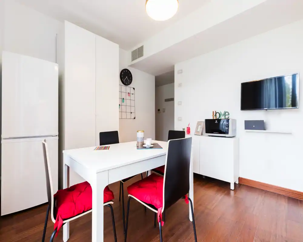 Bright, modern dining area with a white table, four chairs cushioned in red, and compact storage; ideal for a small apartment meal space.