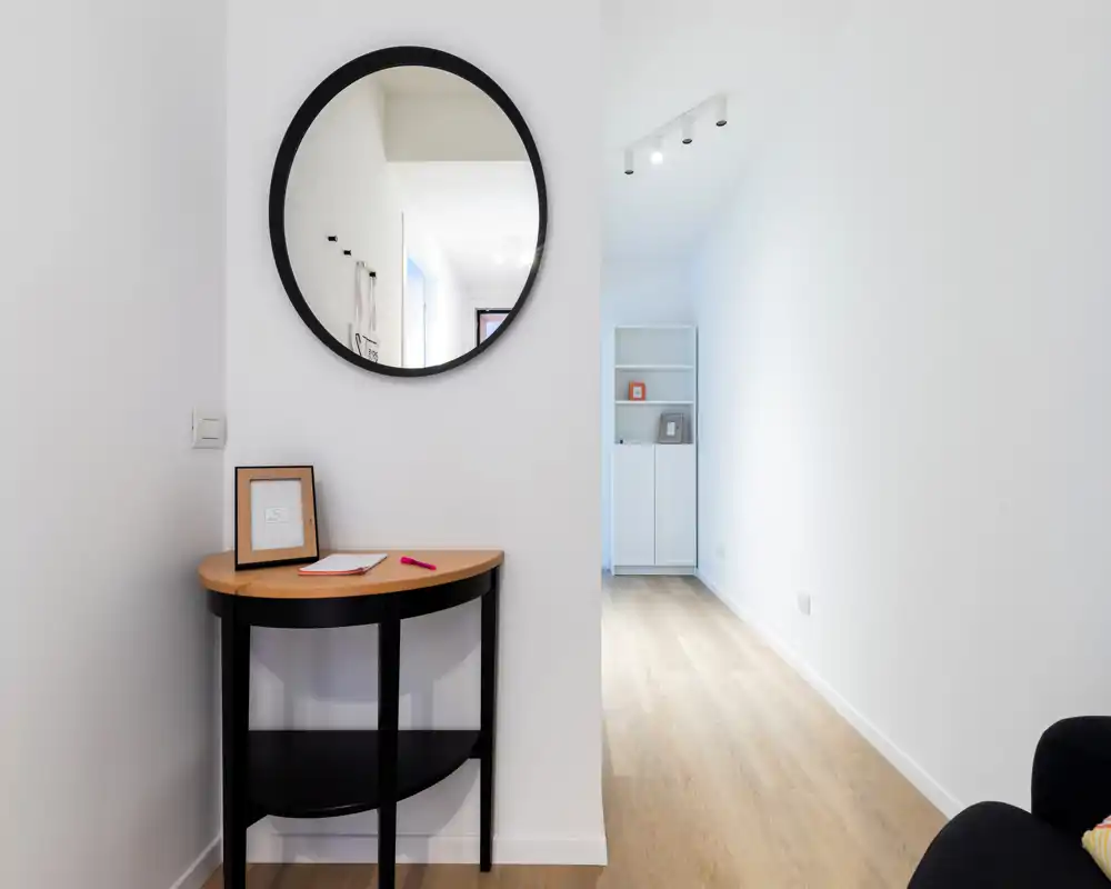 Bright, minimal entryway with a round mirror and a small console table on light wood flooring — a tidy welcoming foyer.
