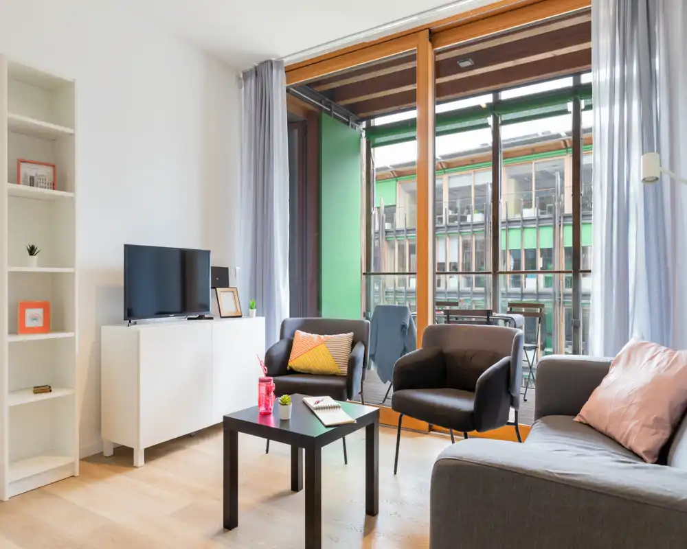 Soggiorno moderno e luminoso con divano e due poltrone, mobile TV e tavolino, che si apre su un balcone tramite grandi porte-finestre.