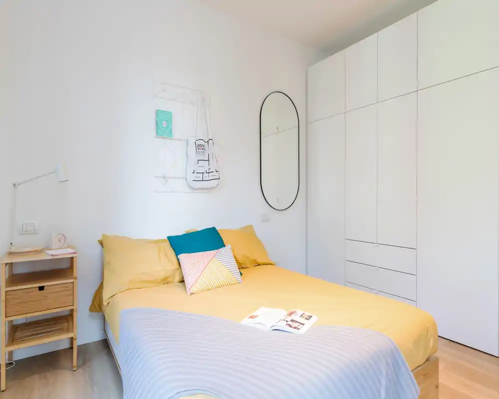 Dormitorio moderno y luminoso con cama doble, cojines coloridos y armarios empotrados blancos. Estilo limpio y acogedor, perfecto para fotos de alquiler.