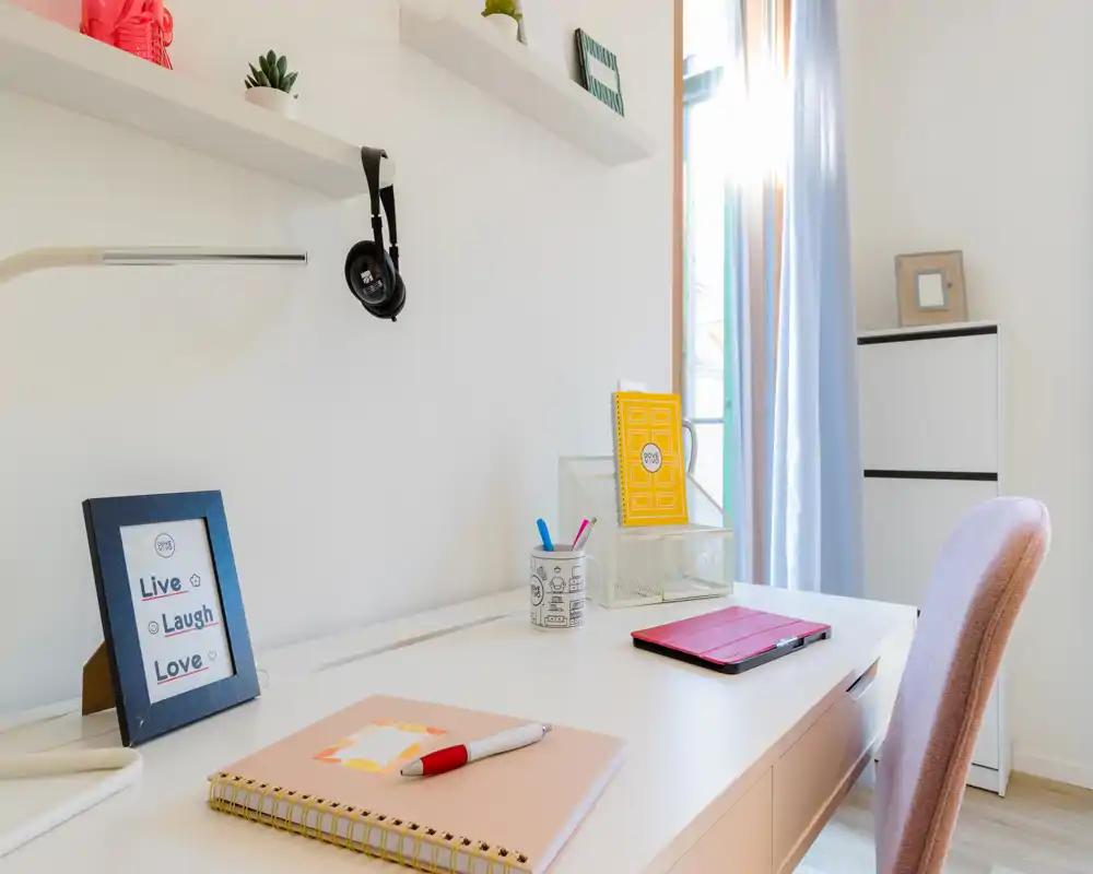 Rincón de estudio luminoso y ordenado con escritorio blanco, silla rosa y material organizado, ideal para teletrabajo o estudio.