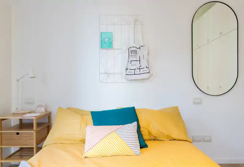 Dormitorio luminoso y moderno con cama amarilla bien hecha, cojines coloridos y mobiliario minimalista — ideal para fotos de alquiler.